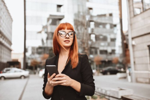 elegant businesswoman arranging meeting on smartphone while walking in city - fashion stock pictures, royalty-free photos & images