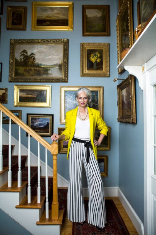 elegant woman in a fashionable outfit with grey hair standing in a staircase with oil paintings on the wall. - fashion stock pictures, royalty-free photos & images