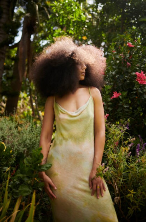 elegant woman with a large afro, wearing a slip dress standing in a lush garden - fashion stock pictures, royalty-free photos & images