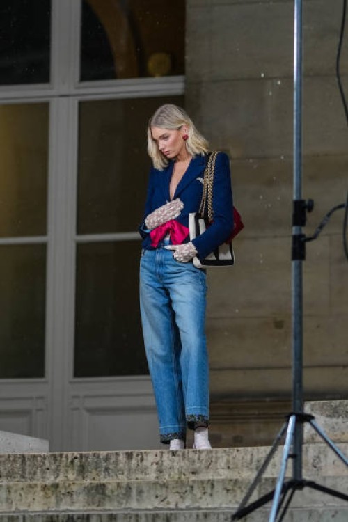 Elsa Hosk wears dark blue blazer jacket, white black pattern bag, navy blue washed denim jean pants, white sneaker shoes, outside Valentino, during...