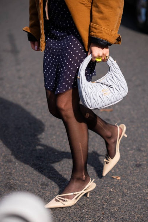 Emili Sindlev wears a beige top and cardigan, blue polka dot mini skirt, brown Carhartt jacket, gret Miu Miu bag and beige kitten heels, outside Miu...