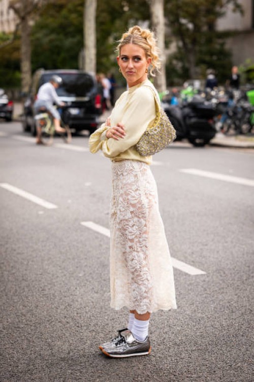 Emili Sindlev wears a yellow sweater, cream lace midi skirt, silver sneakers and yellow bag with silver metal details, outside Rabanne, during the...