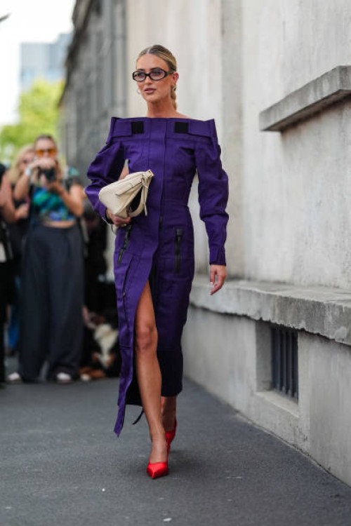 Emili Sindlev wears black glasses, dark purple long sleeve half zipped midi dress, shiny bright red heels, outside Prada, during the Milan Fashion...
