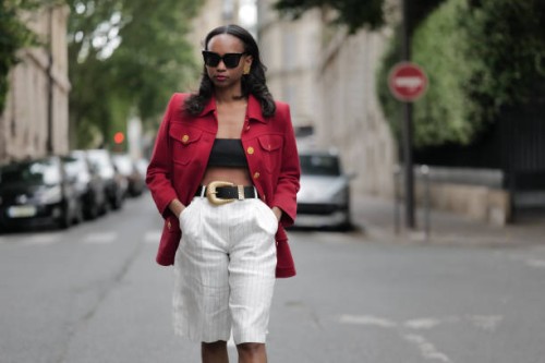 Emilie Joseph wears sunglasses, a red oversize blazer jacket with golden buttons, black bras / crop top, a black leather belt with large golden...
