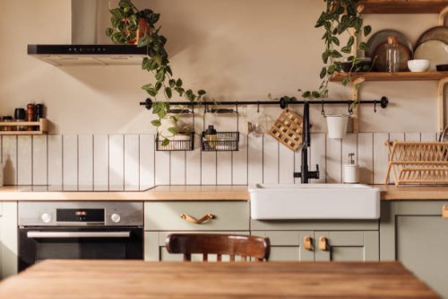 empty kitchen island with marble surface in foreground, green vintage countertop with drawers and pendant lights hanging above, lots of flowers in jars, blurred background - home decoration stock pictures, royalty-free photos