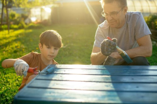 enfant avec grand-père peignant un banc en bois à l’extérieur dans la cour arrière le soir ensoleillé. rénovation de meubles anciens. concept de durabilité. - garden decoration photos et images de collection