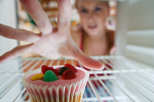 england, cornwall, young woman reaching for cupcake into fridge, focus on hand - junk food stockfoto's en -beelden