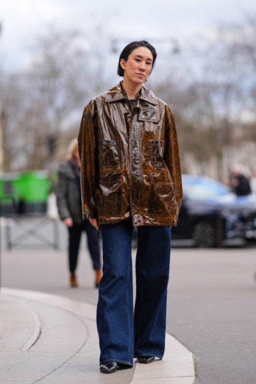 Eva Chen wears a brown shiny leather oversized jacket , blue flared denim pants / jeans , outside Miu Miu , during the Womenswear Fall/Winter...