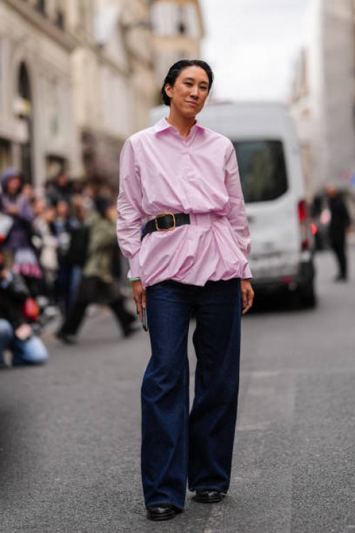 Eva Chen wears a light pink gathered shirt, a black leather belt, dark blue denim jeans / pants, black leather shoes, outside Sacai, during...