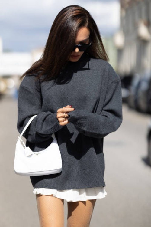Evangelie Smyrniotaki is seen wearing black sunglasses, a white Prada bag, a grey oversized long sleeves sweater and a white mini skirt outside the...