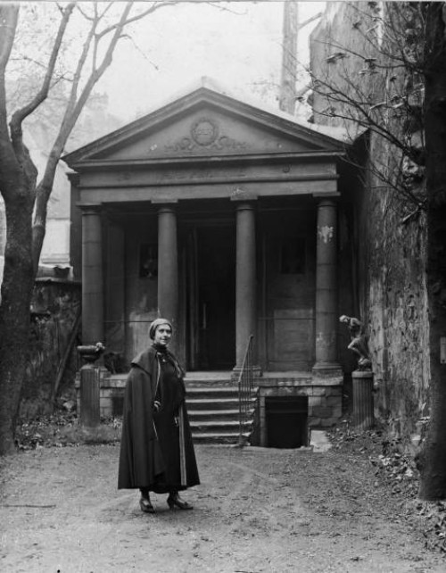 Ex-patriate American author and salon hostess Natalie Clifford Barney wears a cape and stands in front of a Greek-style temple in the garden of her...