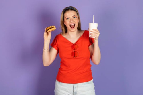 excited hungry pretty girl eats fast food, cheap burger, holds a cheeseburger and soda, open mouth. fast food and unhealthy diet. isolated on purple background. - junk food stock pictures, royalty-free photos & images