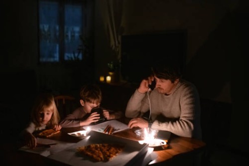 family sitting at home with candles and eating pizza during blackout. children are drawing, man is man is talking by smartphone. energy crisis concept. - junk food stock pictures, royalty-free photos & images