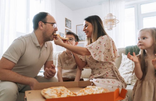 family with two children eating pizza in front of the tv in living room at home - junk food stock pictures, royalty-free photos & images