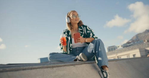 fashion, music and woman with phone in city listening to audio, radio and track in skate park. headphones, summer and female person relax outdoors on smartphone for social media, online and internet - fashion stock pictures, 