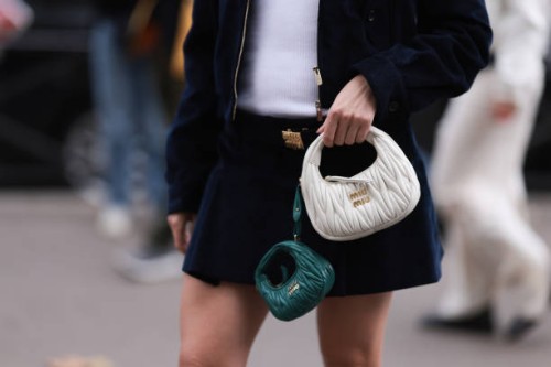 Fashion Week Guest is seen wearing a dark blue jacket, with a dark blue skirt, a Miu Miu belt in gold and a white Miu Miu leather Hobo handbag...