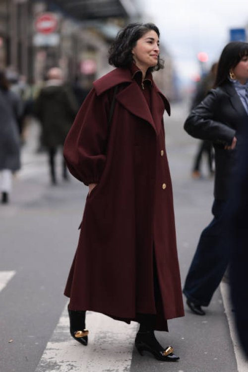 Fashion week guest is seen wearing a long Bordeaux red wool coat with big collar and big sleeves, gold buttons, black tights and black high patent...