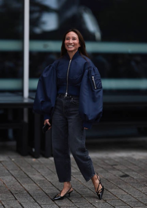Fashion Week guest is seen wearing a shiny blue cropped bomber jacket with puffy sleeves; grey jeans with straight leg and mid-heeled, pointed, black...