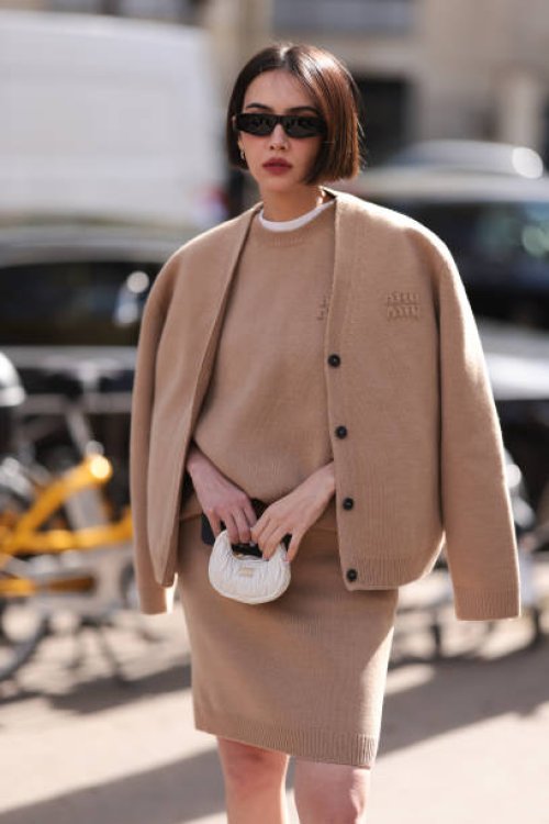 Fashion Week Guest is seen wearing a white T-shirt, a beige sweater by Miu Miu, a beige knit jacket by Miu Miu, a beige knit skirt, silver creoles,...