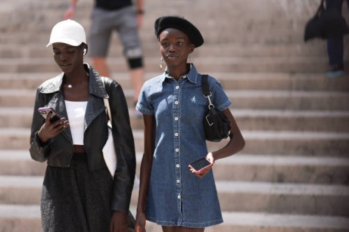 Fashion Week guest is seen wearing a white cap, a black leather jacket, underneath a white top, a fluttering skirt and white sneakers. The guest...