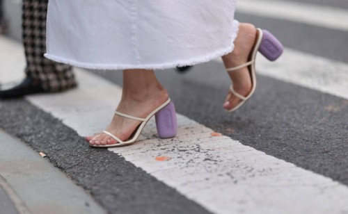 Fashion Week guest is seen wearing an ankle-length white denim skirt with frayed hem, and cream-white leather sandals with two straps and lilac block...