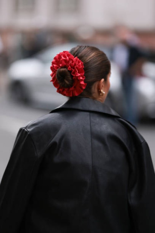 Fashion Week guest is seen wearing golden earrings, a shiny red ruffled scrunchie, and a black leather jacket before the Gestuz Show during the...