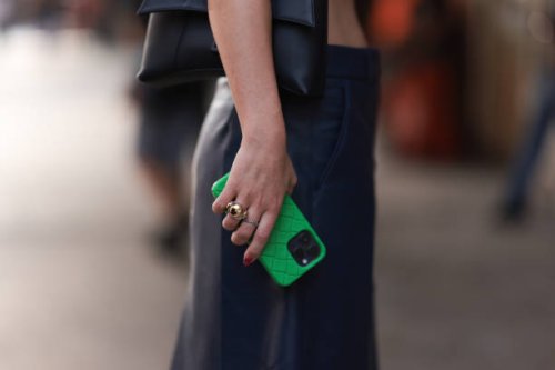 Fashion Week guest is seen wearing red shell earrings, a blue/white cropped top, underneath a second white cropped top, a black bag from Balenciaga,...