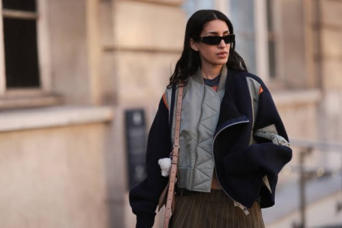 Fashion Week Guest seen wearing a short brown stripped skirt, grey shirt, black sunglasses, black, orange and khaki oversized jacket and a brown Acne...