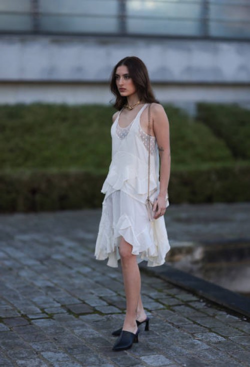 Fashion Week Guest seen wearing a white dress, transparent top with dots, black sandals heels and beige bag outside Stella McCartney show, during the...