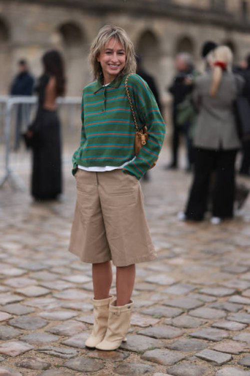 Fashion week guest was seen wearing beige shoes, beige shorts, a brown bag and a green pullover with collar and red stripes before the Loewe Fashion...