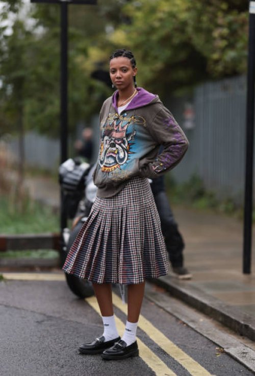 Fashion Week Guest was seen wearing black leather loafer, white Holzweiler socks, braids, a green and brown skirt, a white tank top and a grey-brown...