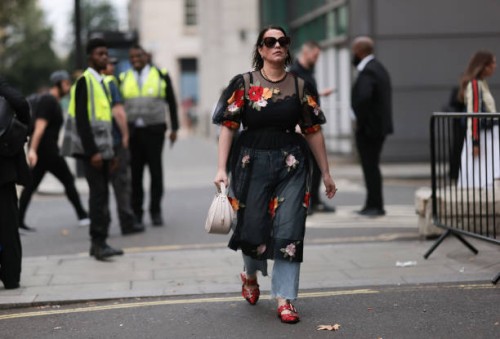 Fashion Week Guest was seen wearing red leather shoes, a denim jeans, abbeige bag, dark shades, a black top under a black transparent dress with...