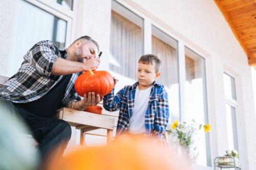 father and son drawing jack on pumpkin for halloween in the back yard of house - garden decoration stock pictures, royalty-free photos & images