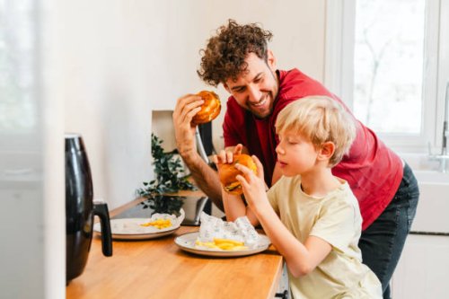 father and son eating hamburger at home - junk food stock pictures, royalty-free photos & images