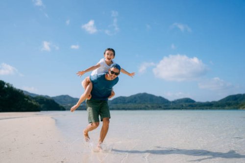 father giving piggyback ride to young daughter on beach, japan - travel stock-fotos und bilder