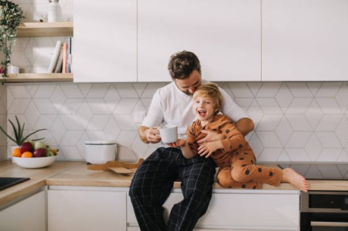 father sitting on kitchen counter with his little son and having morning coffee. - food stock pictures, royalty-free photos & images