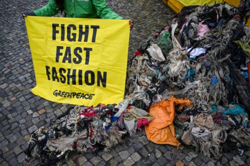 February 2024, Berlin: Greenpeace activists protest at the Brandenburg Gate against the pollution of the environment in Ghana caused by fast fashion...