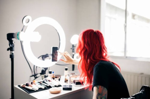 female artist with dyed red hair using smart phone while vlogging at studio - fashion stock pictures, royalty-free photos & images