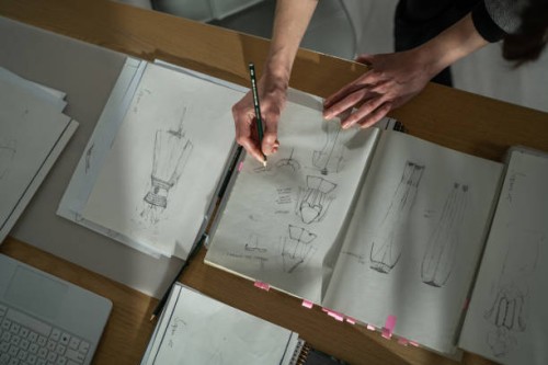 female atelier sitting at table in studio and drawing new fashion models - fashion stock pictures, royalty-free photos & images