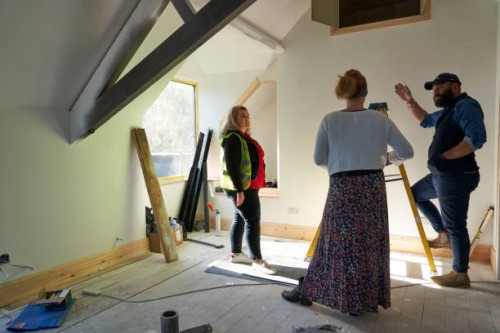 female builder in an attic building site stands with another builder and the client discussing the project. they stand in the attic / roof space with exposed roof beams - home decoration stock pictures, royalty-free photos 