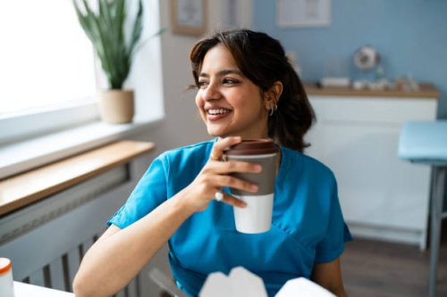 female doctor indian ethnicity in blue medical scrubs having a lunch break at the ordination - junk food stock pictures, royalty-free photos & images