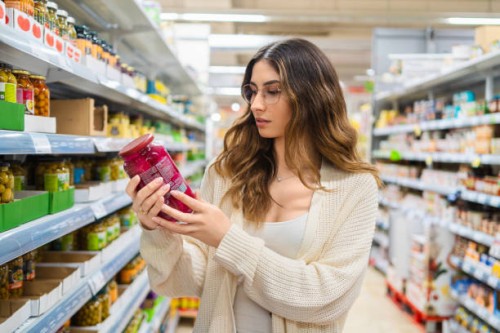 female professional studying product label, wearing eyeglasses in grocery store aisle, surrounded by packaged foods, comparing nutritional details - food stock pictures, royalty-free photos & images