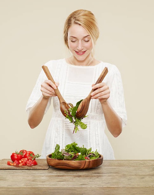 female smiling as she tosses a fresh salad - food stock pictures, royalty-free photos & images