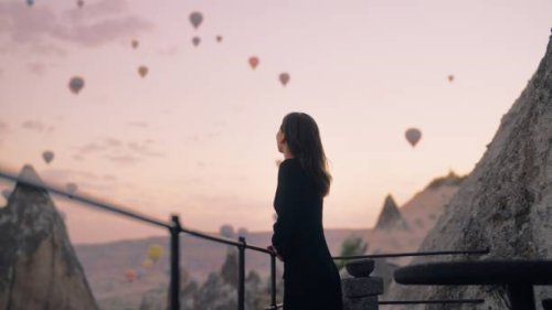 female tourist enjoying watching hot air balloons flying in the sky at rooftop of hotel where she is staying during her vacation - travel stock pictures, royalty-free photos & images