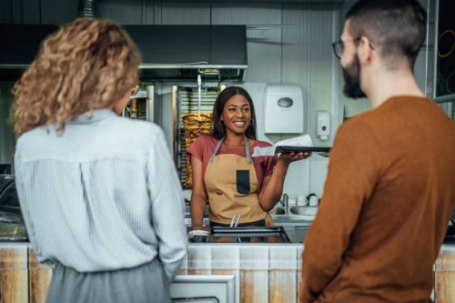 female worker giving orders to customers in a fast food restaurant - junk food stock pictures, royalty-free photos & images