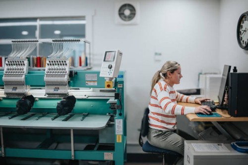female worker using computer while operating embroidery machine - fashion stock pictures, royalty-free photos & images