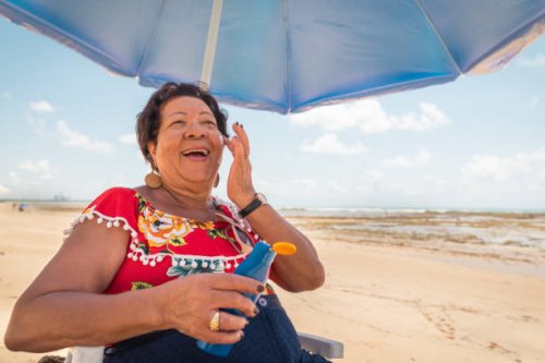 femme aîné utilisant une lotion de bronzage sur la plage - hairstyle photos et images de collection