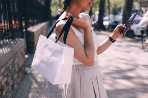 femme élégante utilisant un smartphone et transportant des sacs à provisions - fashion photos et images de collection
