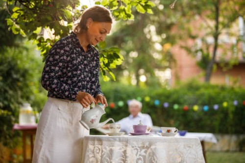 femme mûre heureuse versant du thé dans une tasse de thé sur une table dans la cour arrière - garden decoration photos et images de collection