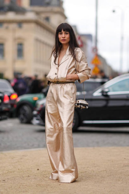 Fer Millan wears a golden shiny full look, a jacket with gathered sleeves, flared pants , a belt, a Chanel bag, outside Chanel, during the Womenswear...